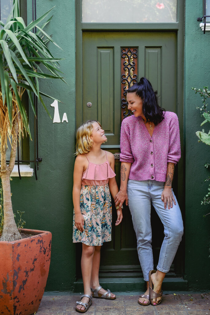 Mother and daughter smiling at each other while standing in front of a green door.
