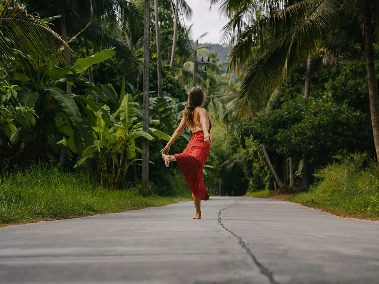 Woman in red dress dancing on a street with palm trees