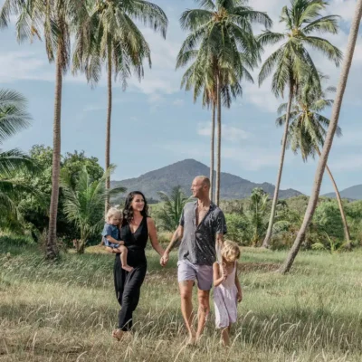 Family of four holding hands, palm trees in the background. Koh Phangan Family Itinerary