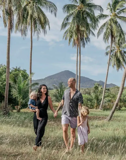 Family of four holding hands, palm trees in the background. Koh Phangan Family Itinerary