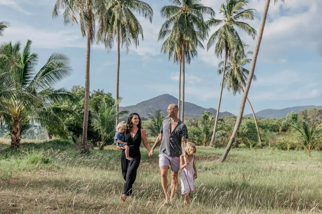 Family of four holding hands, palm trees in the background. Koh Phangan Family Itinerary