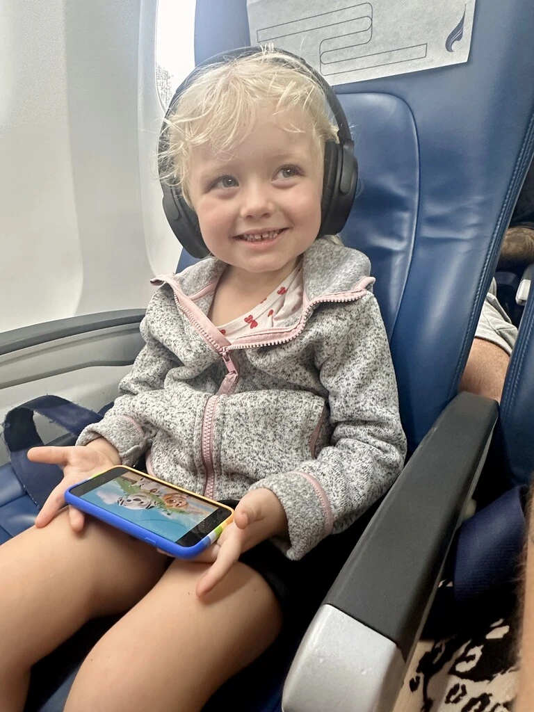 Little girl with phone and headphones in plane, How to Travel With a Toddler on a Plane