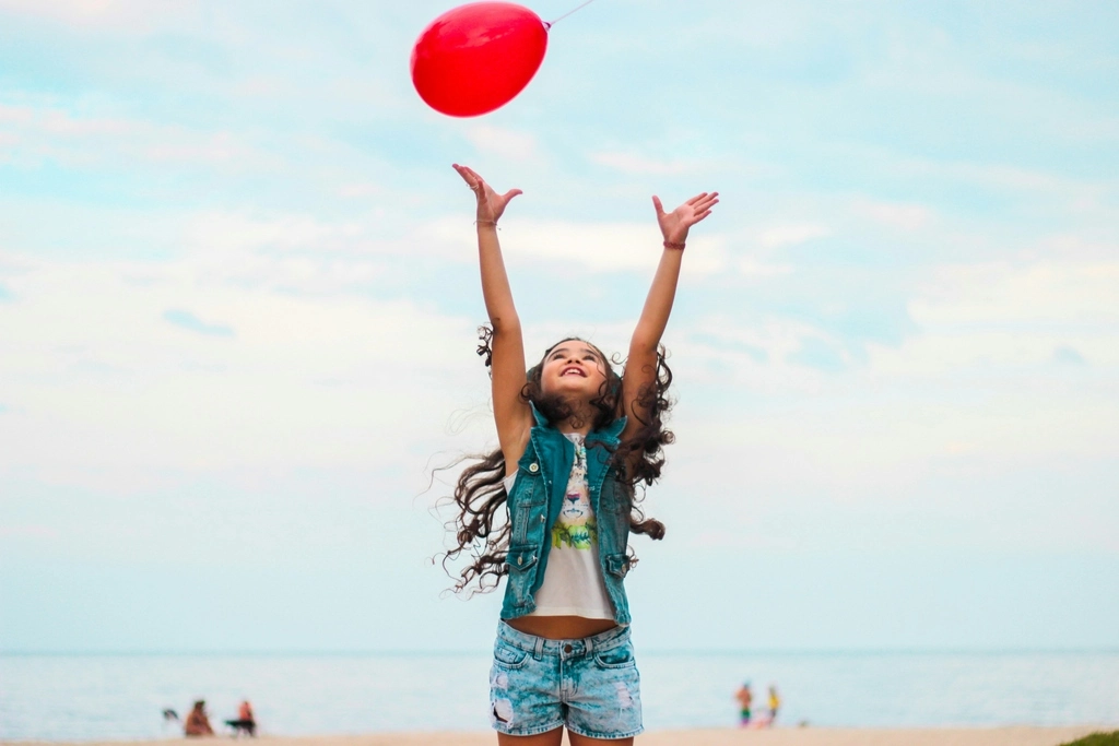 Girl playing on the beach with a red balloon, 50 Must-Try Beach Activities for Kids That Will Inspire You