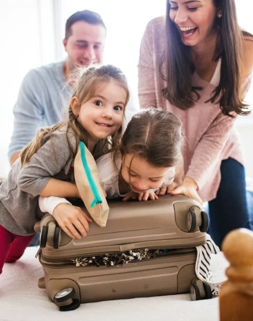 Family of four trying to close a big suitcase.