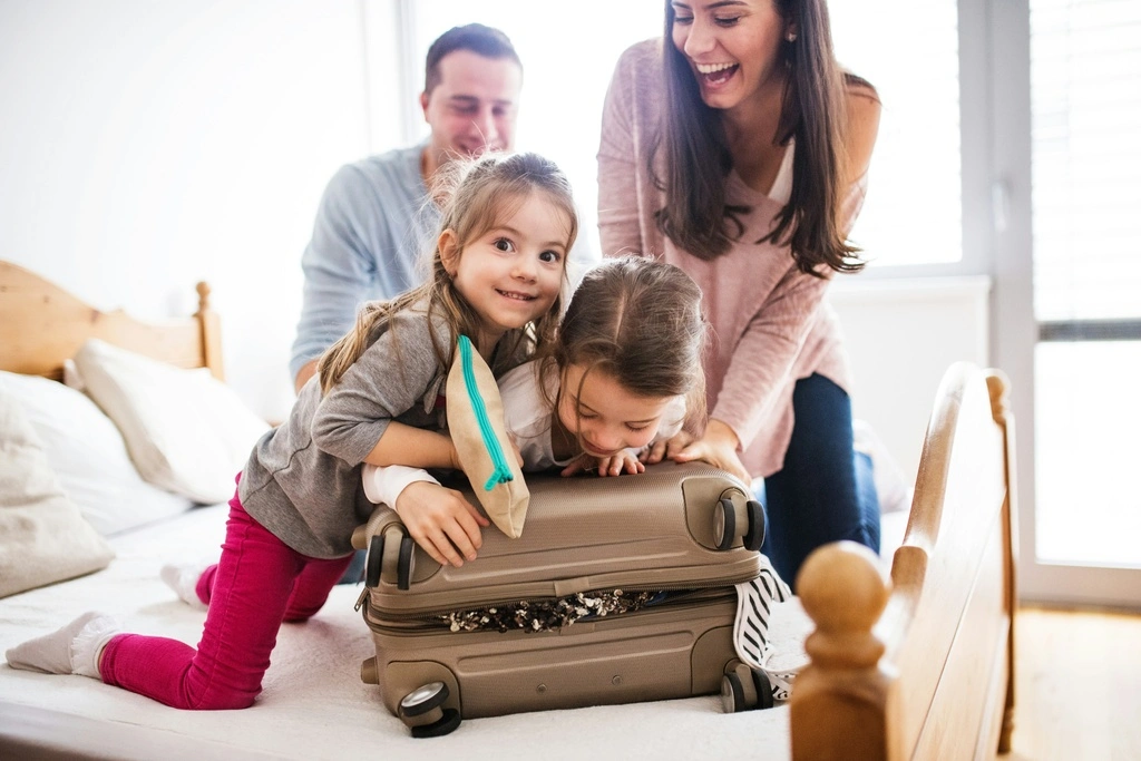 Family of four trying to close a big suitcase.