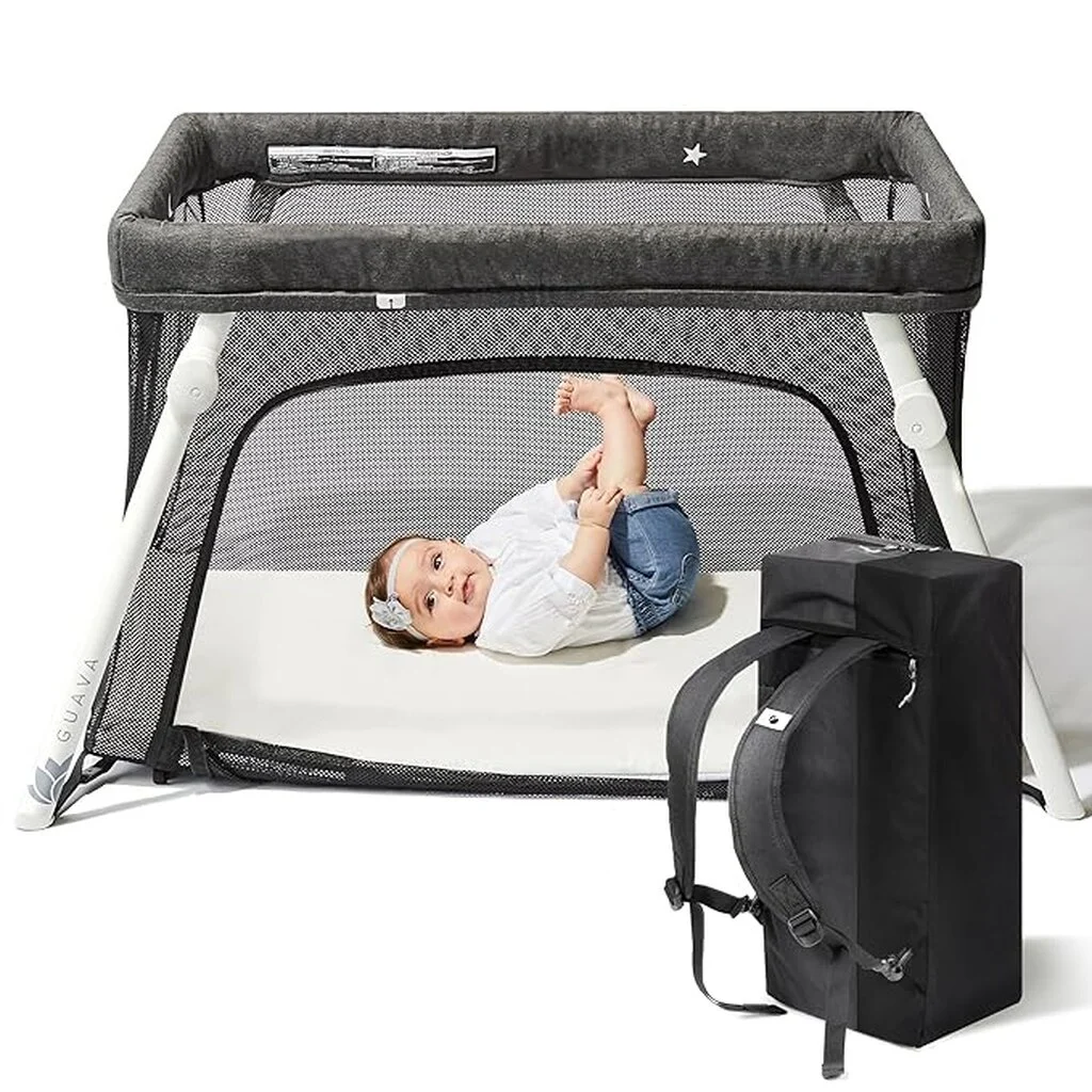 High-walled travel crib in dark grey with a young toddler laying inside.