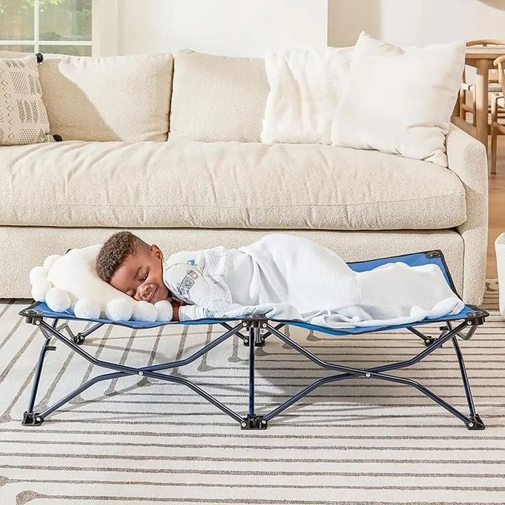 Little colored boy sleeping in a travel toddler bed, covered by a white blanket. Best Travel Toddler Bed