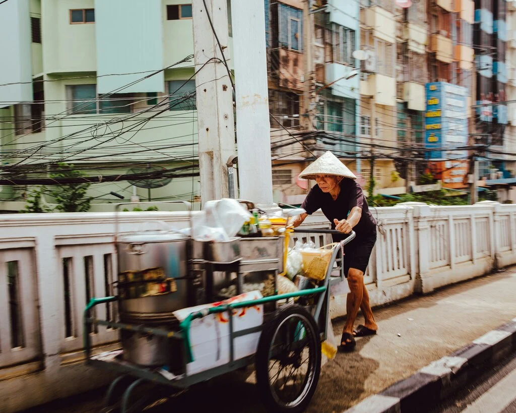 Man in Thailand pushing a street food wagon, vaccines for Thailand travel