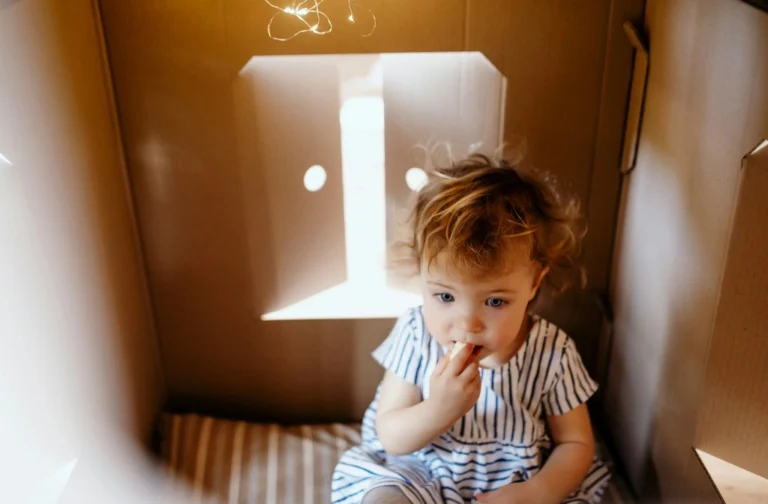 Blond toddler boy sitting in a carton box.