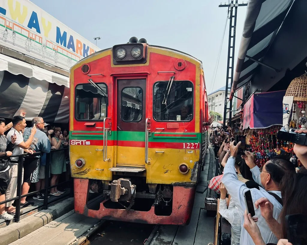 Red and yellow train navigating through narrow road full of people