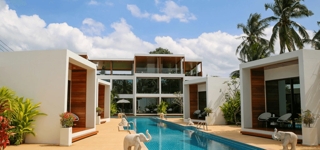 White three-storey hotel building next to a pool with small elephant statues.