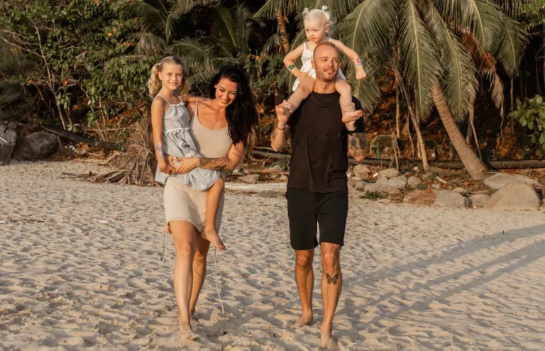 Family of four walking barefoot on the beach, palm trees in the background. How much does it cost to travel the world with a family.