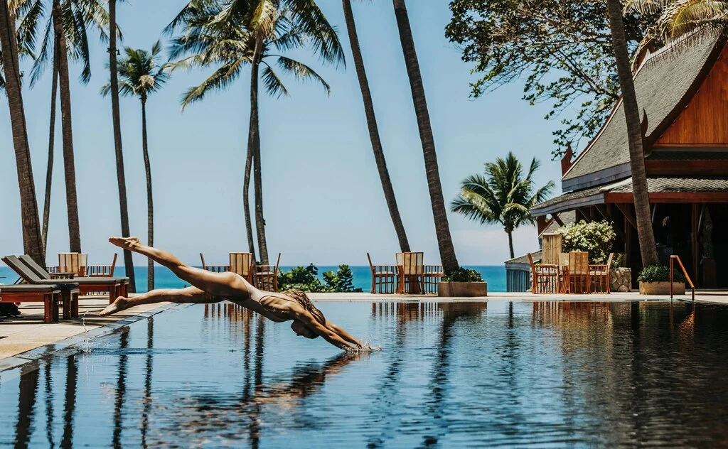 Woman in swimsuit jumping into a huge hotel pool directly at the beach.