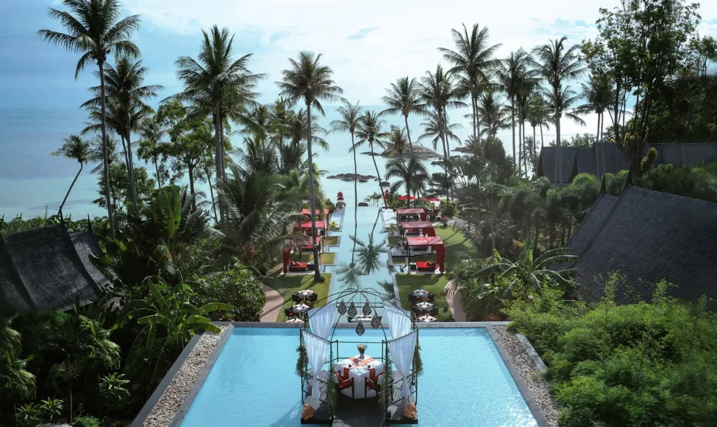 Aerial view of wooden hotel buildings with an infinity sea view pool in the middle.