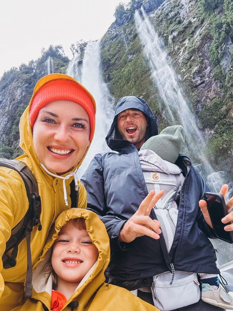 Family of four in rain coats standing in front of a big waterfall. How much does it cost to travel the world with a family?