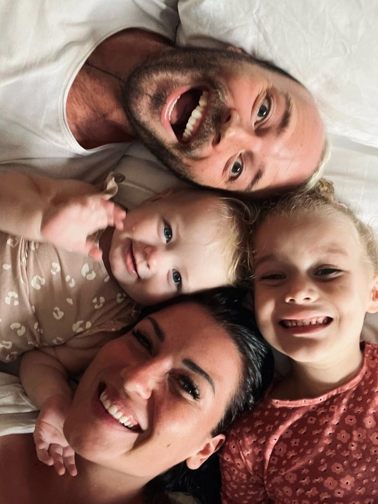 Family of four with a baby and a toddler girl snuggling on a bed. How much does it cost to travel the world with a family