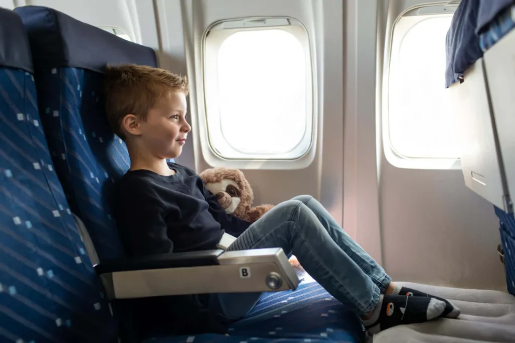 Boy sitting on a plane, resting his feet on a inflatable foot cushion. Airplane beds for kids.