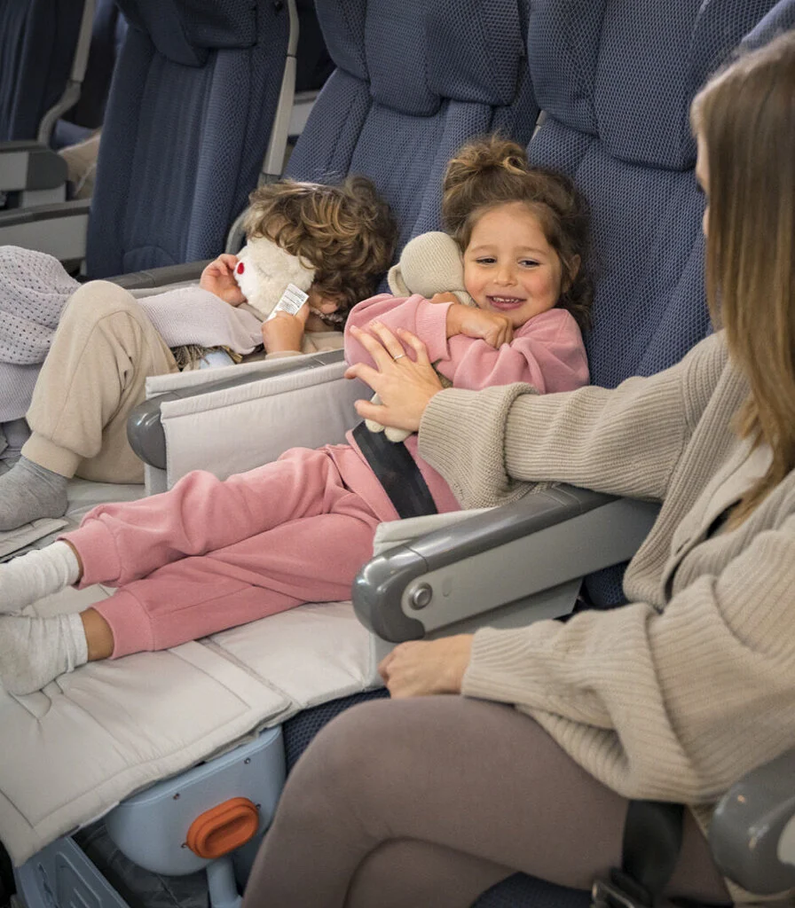 Little girl playing with her mum in the plane while laying on an airplane bed for kids.