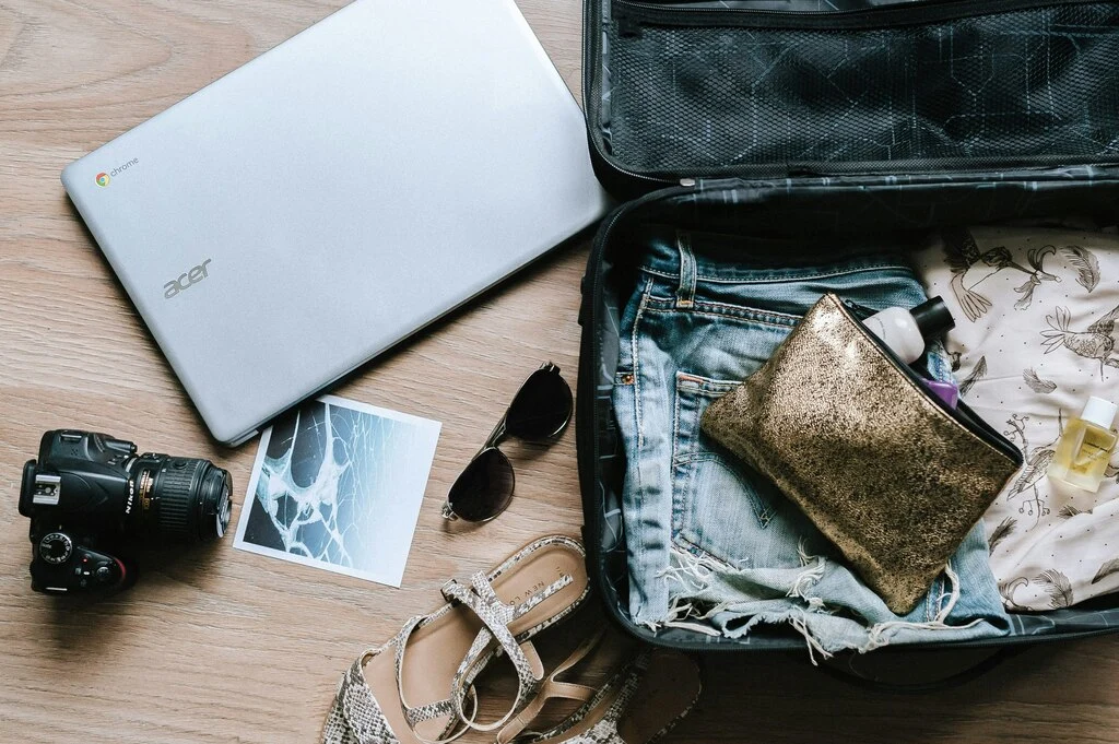 Open suitcase with clothes, laptop, camera and sunglasses. Packing List for Southeast Asia