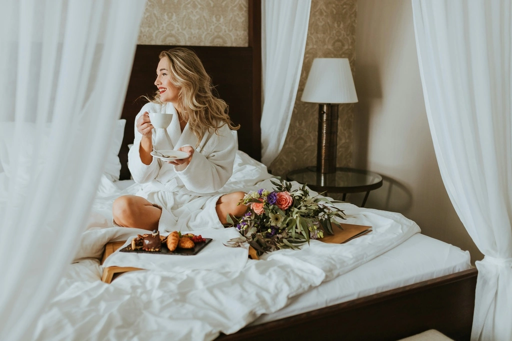 A woman sitting on a bed holding a cup of tea.