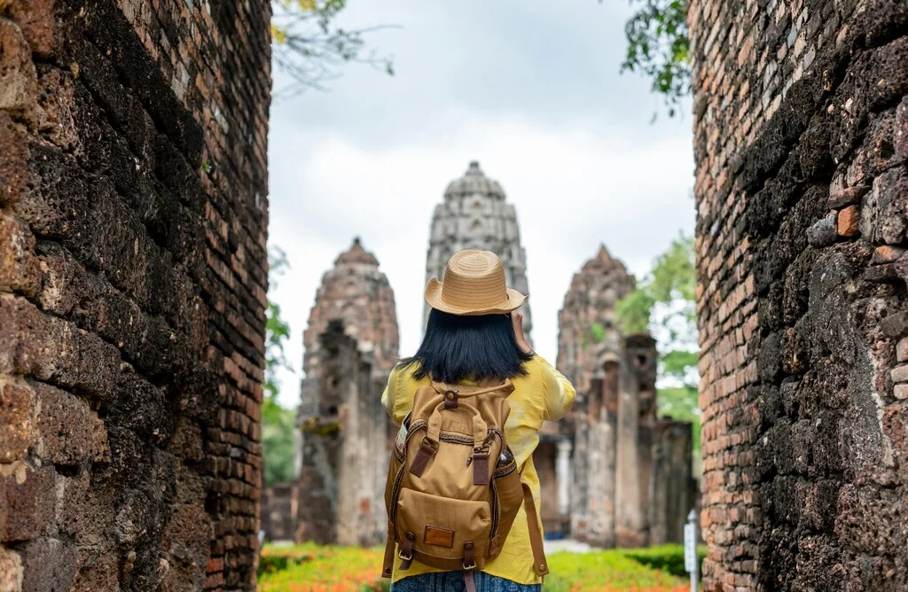 Black-haired woman with hat and backpack walking through the entrance of a temple in Southeast Asia.