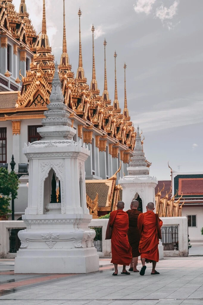 Monks with orange robes in front of white-golden temple buildings.