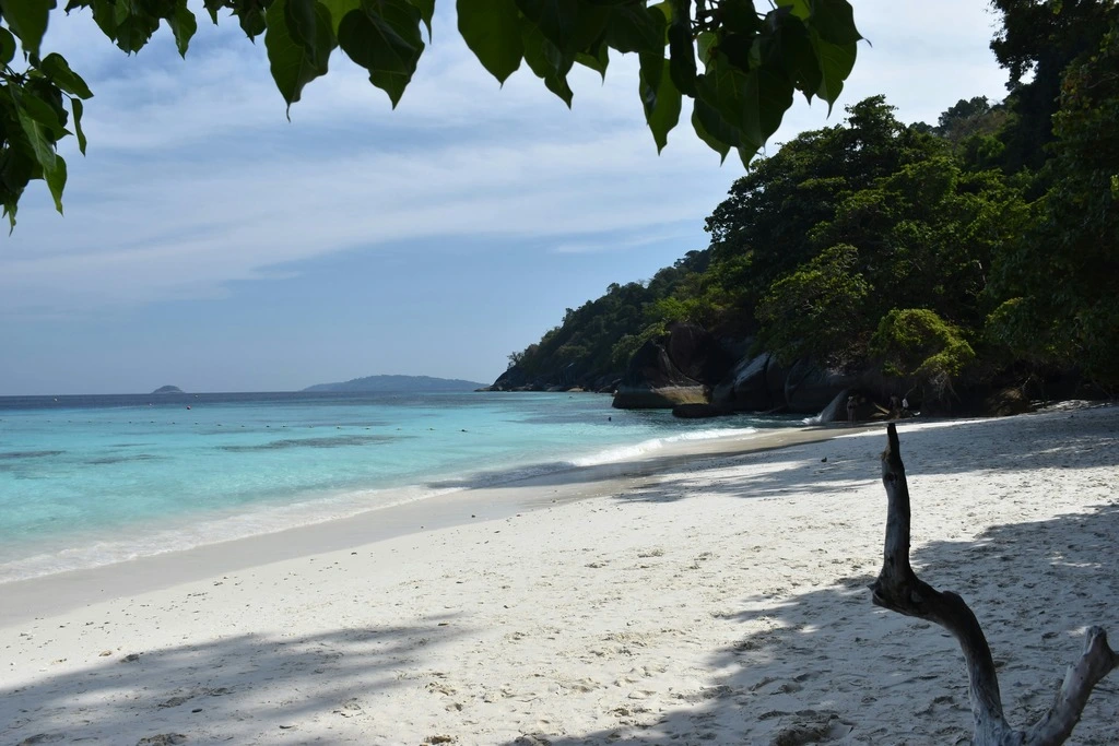 Tropical beach with white sand and green hills in the background.