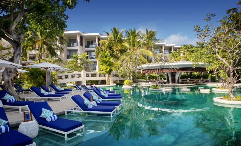 A pool with lounge chairs and umbrellas in front of a building.