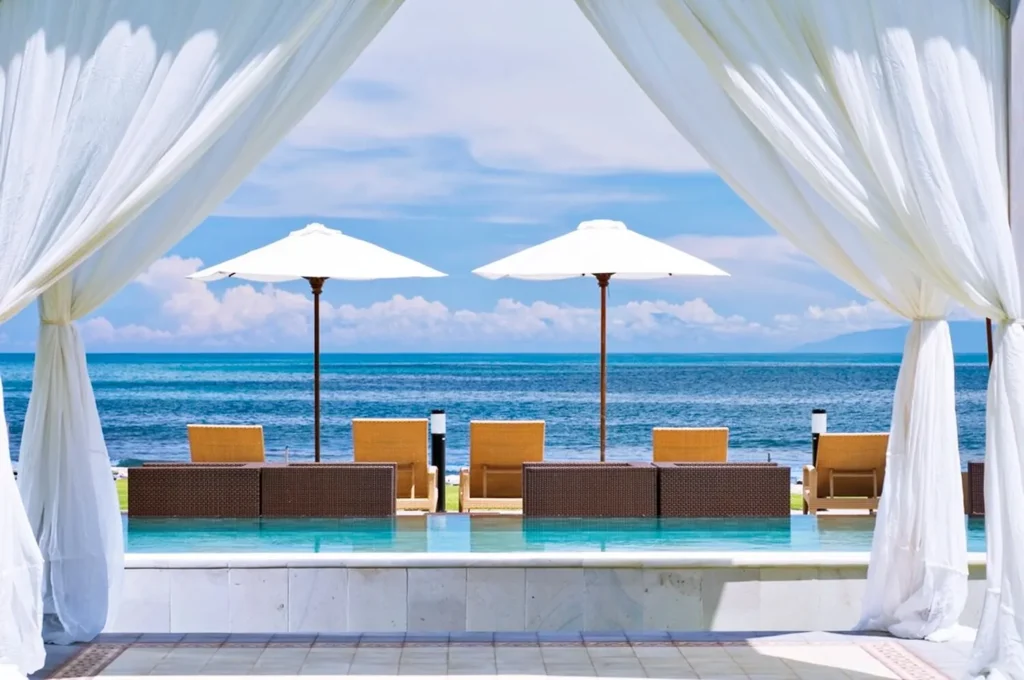 A pool with chairs and umbrellas by the ocean. Best Family Resorts in Bali.