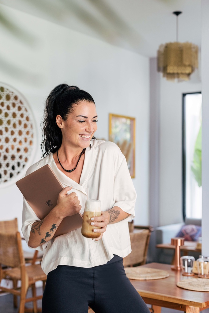 Woman in a cafe with laptop and coffee in her hands.