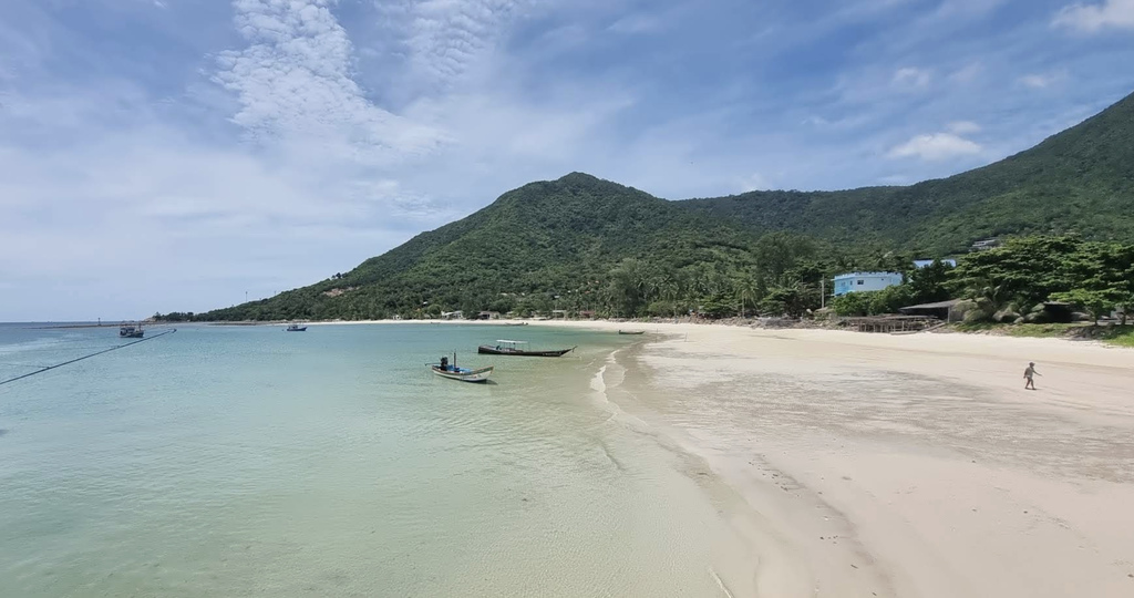 Wide beach will green hills in the background.