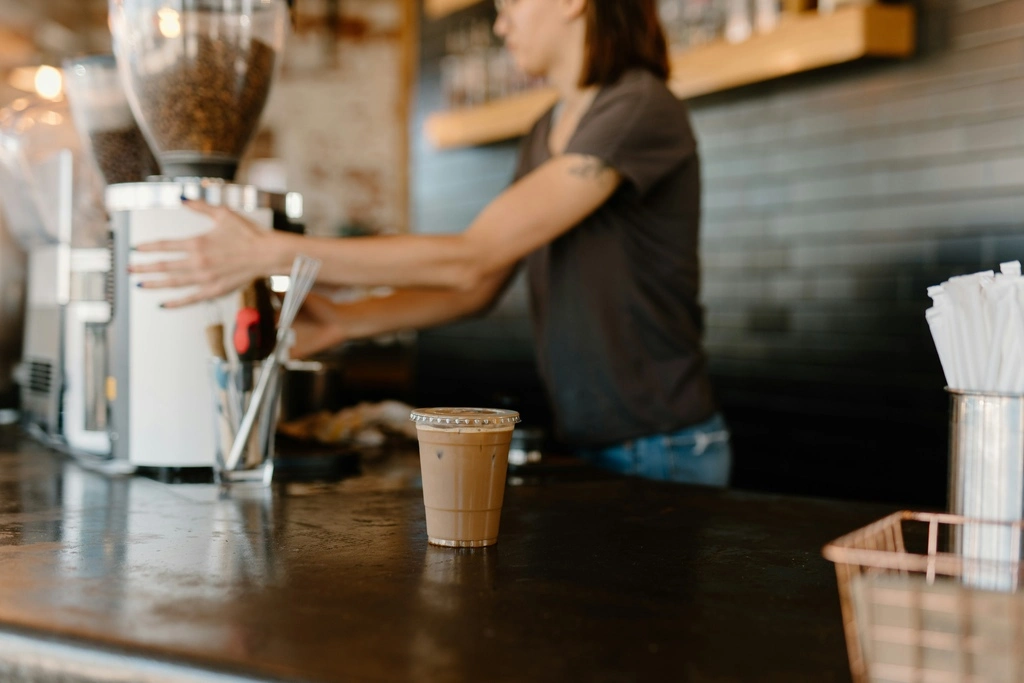 Barista woman preparing a coffee in a plastic cup.