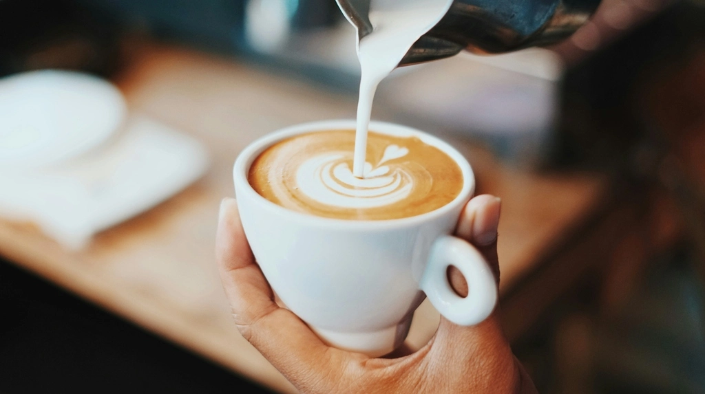 A person pouring milk into a cup of coffee. Thailand Coffee Brands