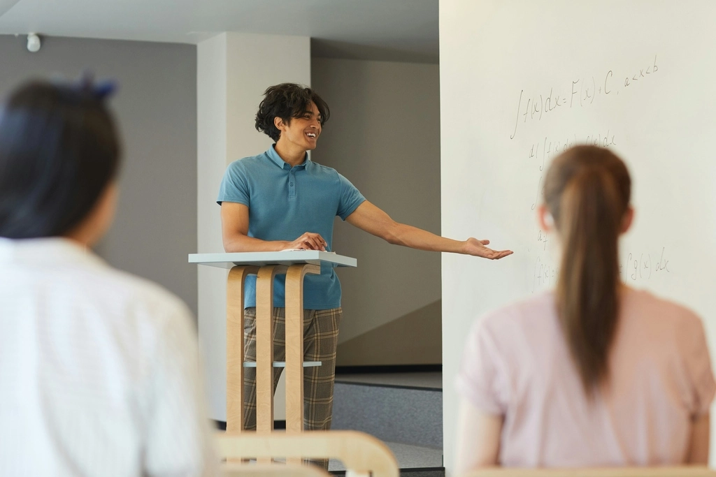 A man standing at a podium in front of his students with his hand out to the side. Expat Jobs in Thailand.