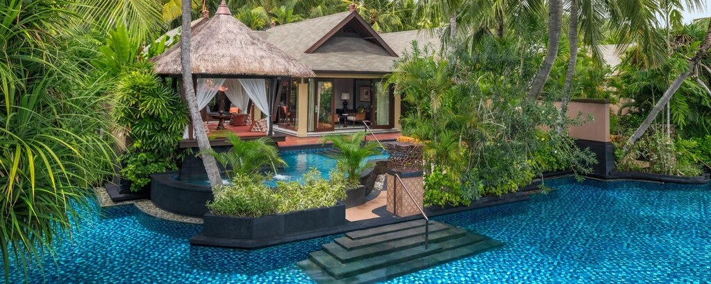 A pool with a building and a thatched roof.