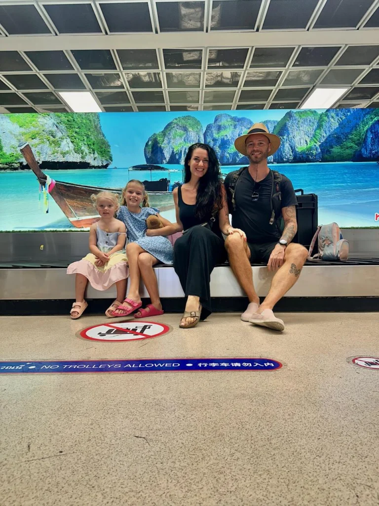 Family of four sitting on the baggage claim belt at an airport.