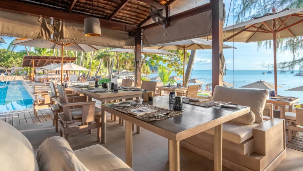A table and chairs outside with a beach in the background.