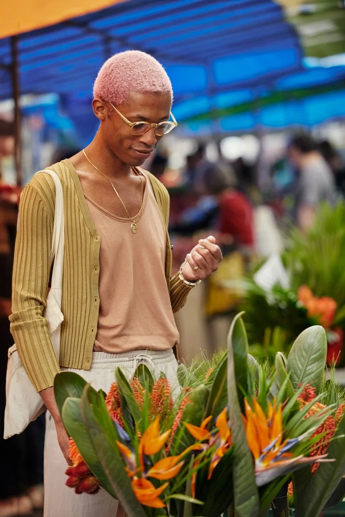 A man with pink hair looking at flowers, and showcasing what to wear in Bangkok.