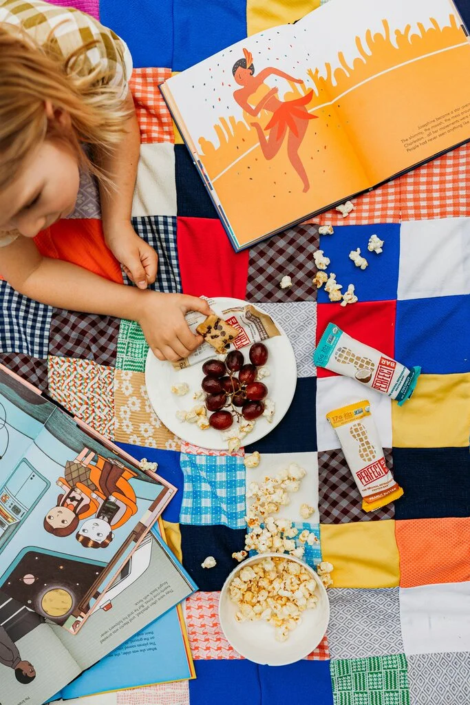 31 Healthy Travel Snacks for Kids (100% Veggie) 23 A child eating popcorn and grapes on a quilt.