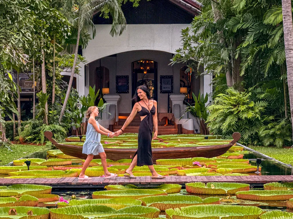 Anantara Bophut Koh Samui – Honest Family Review 2025 39 A woman and child walking on a dock with lily pads in the background.