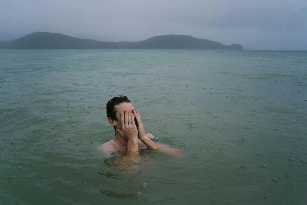 A man in the water with his hands over his face.