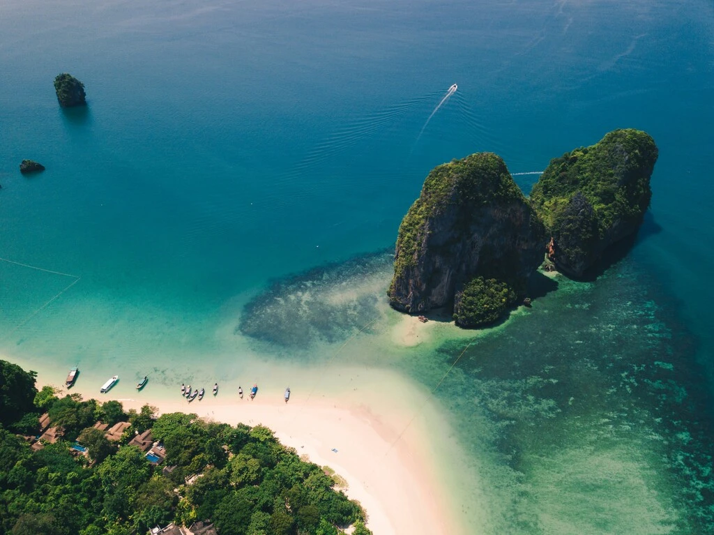 A beach with boats and rocks in the water.