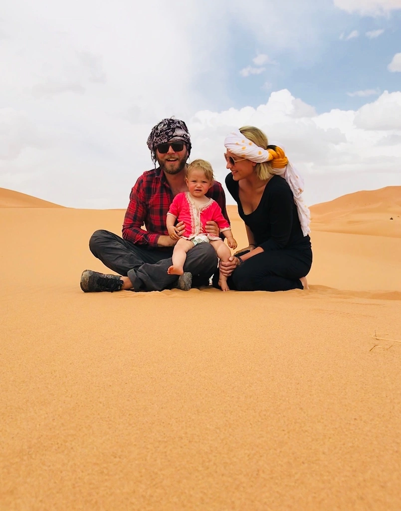 A family of three sitting in sand. Not yet a digital nomad couple.