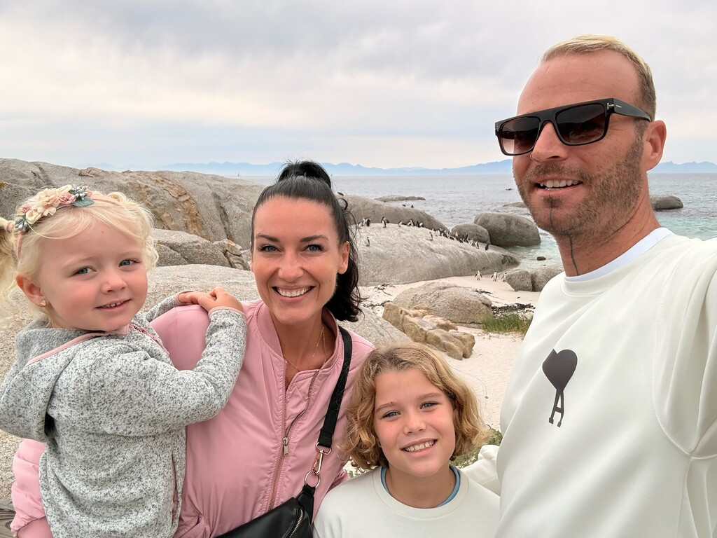 Family posing near penguins by ocean.