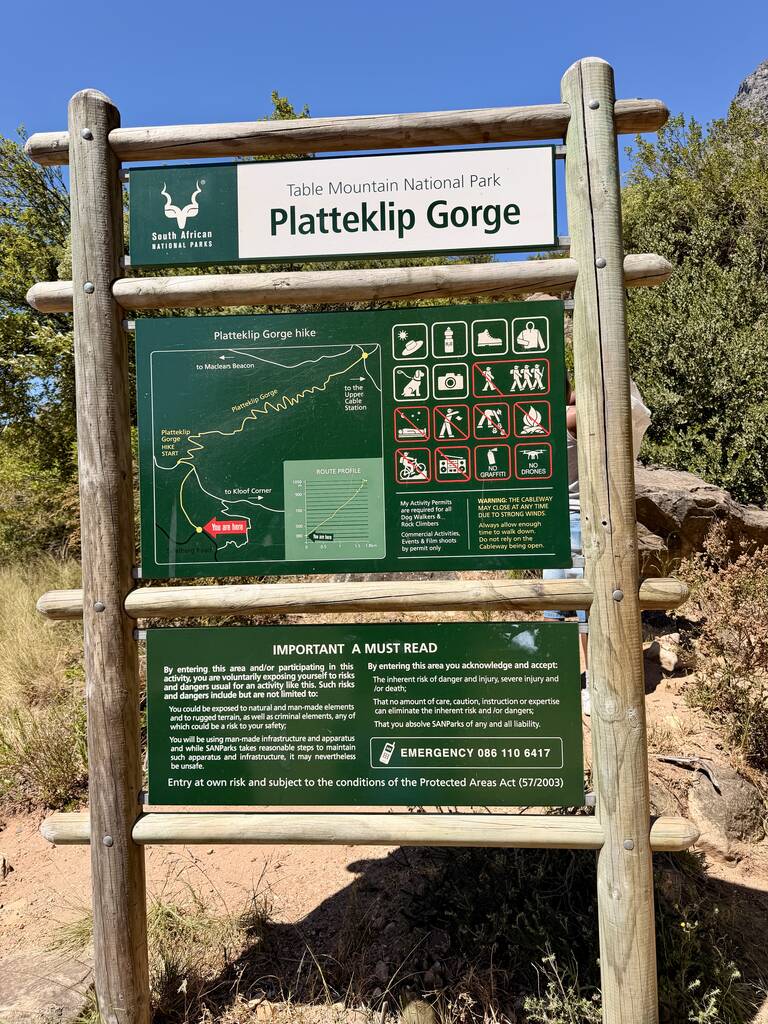 Hiker walking along the road toward Table Mountain in Cape Town with rocky cliffs and trees around.