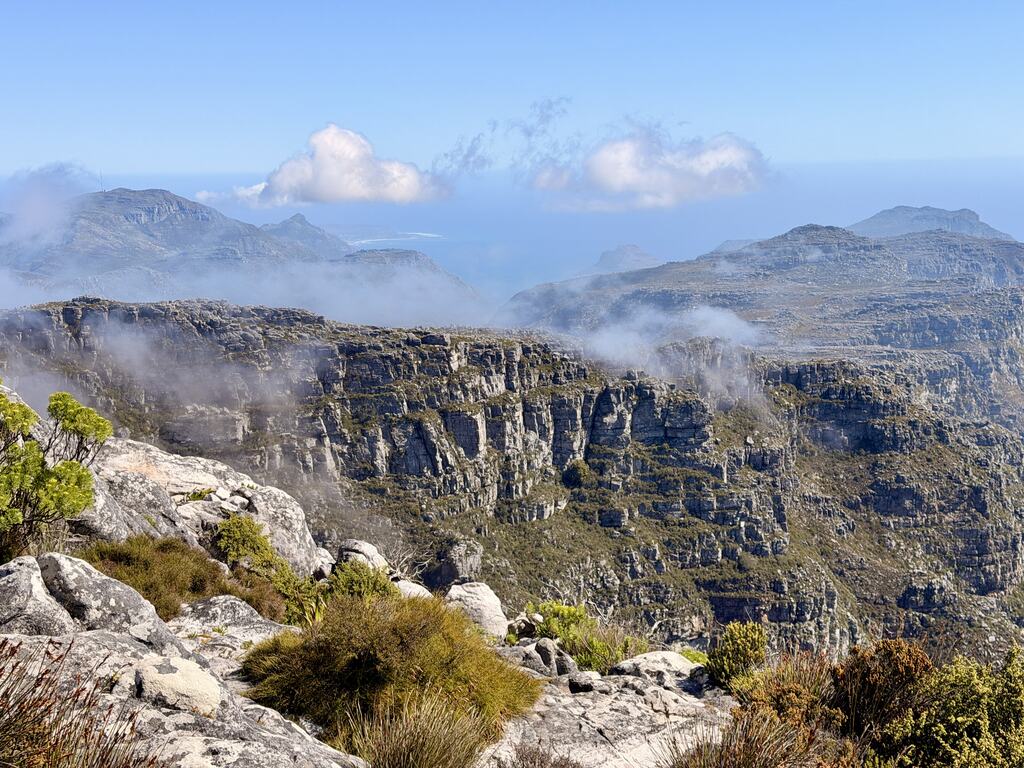 Cliffs and rocky plateau on Table Mountain covered with green vegetation and low clouds drifting over the landscape.