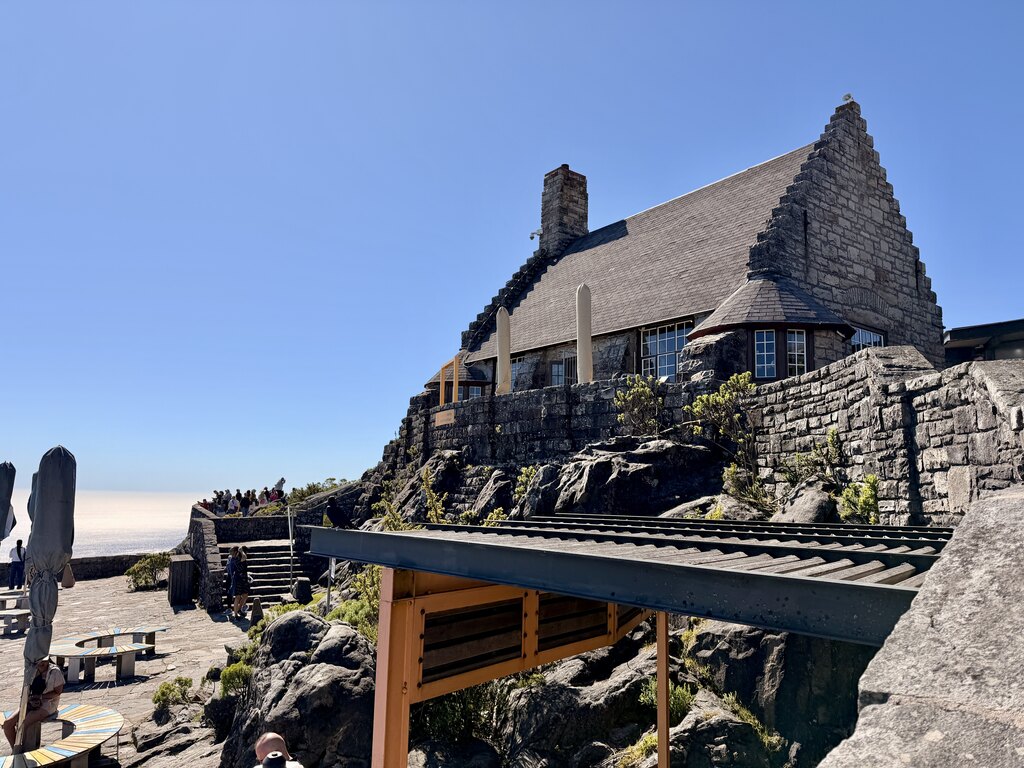 Stone building with steep roof and terrace on top of Table Mountain in Cape Town under a clear blue sky.