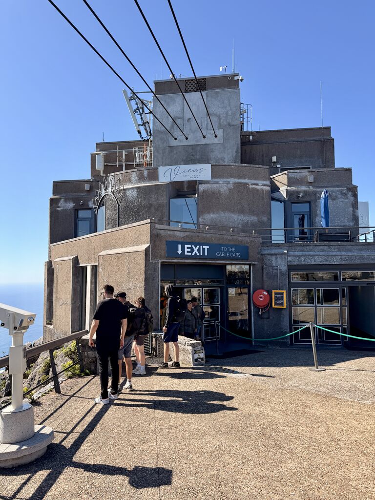 Cable car station on top of Table Mountain with people walking toward the exit under a bright blue sky in Cape Town.