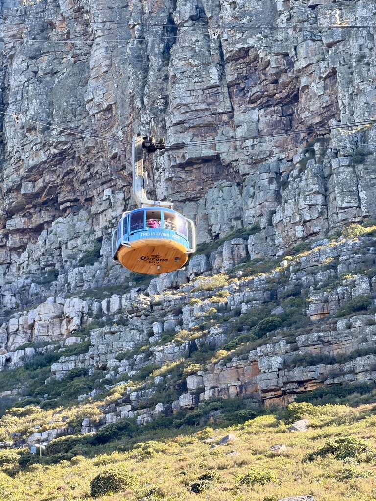 Table Mountain cable car ascending along steep rocky cliffs in Cape Town on a bright sunny day.