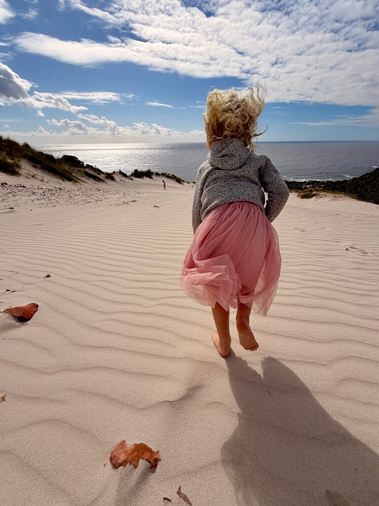 Young girl running down a sandy dune.